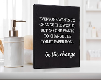 May include: Black wooden sign with white text that reads "Everyone wants to change the world, but no one wants to change the toilet paper roll. Be the change."