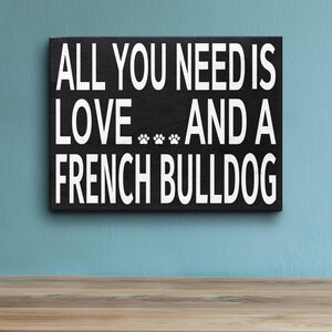 May include: Black wooden sign with white text that reads "All you need is love... and a French Bulldog".