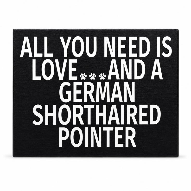 A rectangular black plaque or sign with bold white text reading 'ALL YOU NEED IS LOVE.