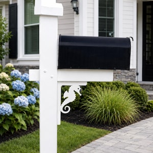 May include: A black metal mailbox mounted on a white wooden post. The post features a decorative white metal bracket shaped like a seahorse, positioned directly underneath the mailbox to provide structural support and visual detail.