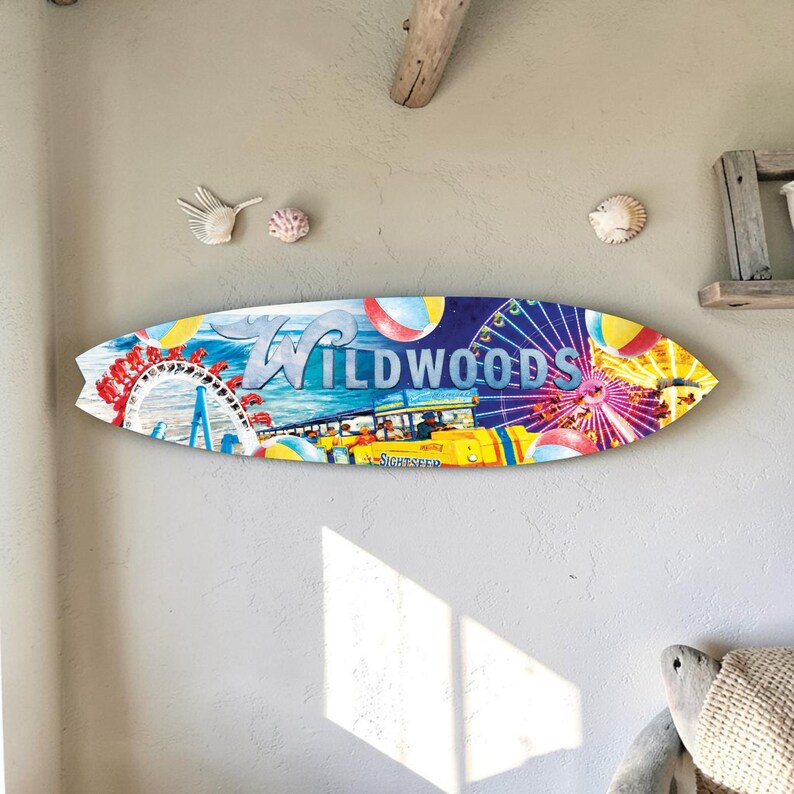 May include: A surfboard-shaped wooden sign with a colorful illustration of Wildwood, featuring a Ferris wheel, beach balls, and a yellow sightseeing bus. The word "Wildwoods" is prominently displayed in blue and white.