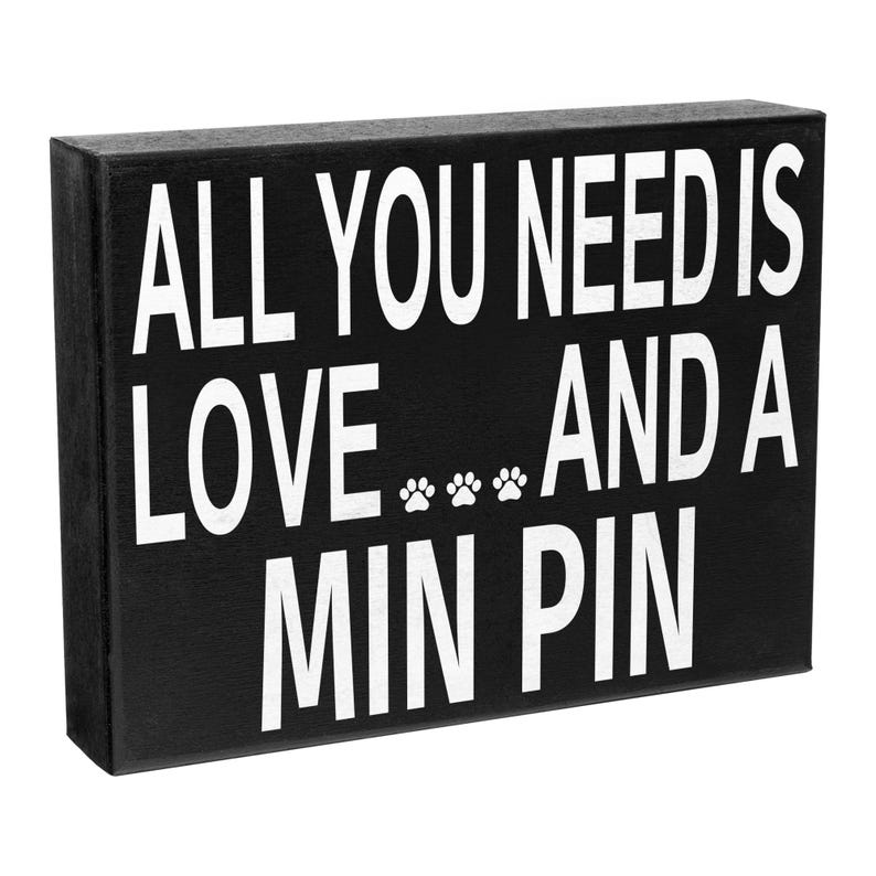 May include: Black wooden sign with white text that reads "All you need is love... and a Min Pin".
