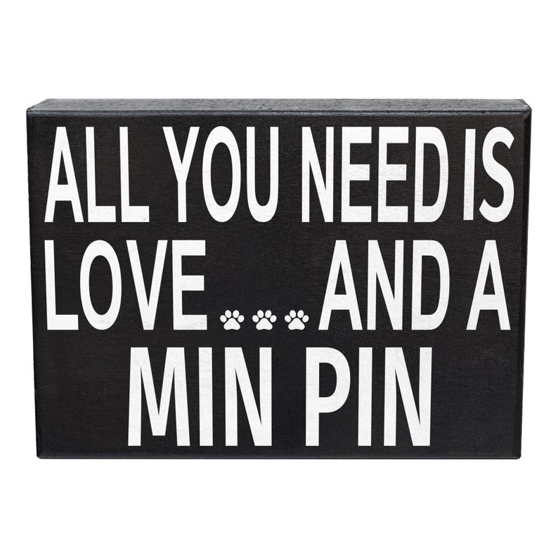 May include: Black wooden sign with white text that reads "All you need is love... and a Min Pin".