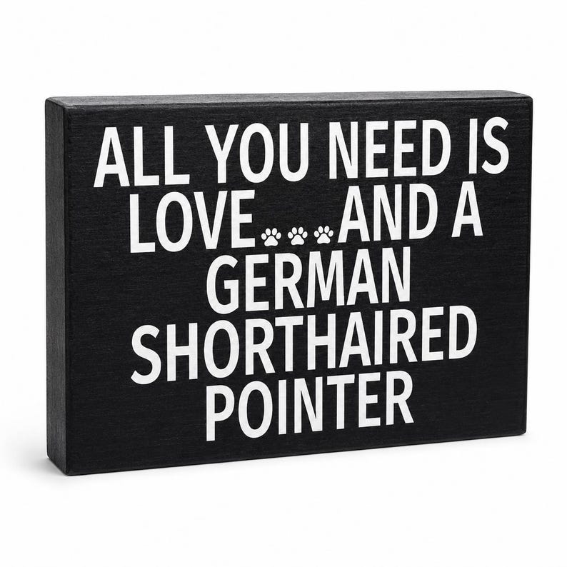 A rectangular black wooden sign with bold white text reading 'ALL YOU NEED IS LOVE.