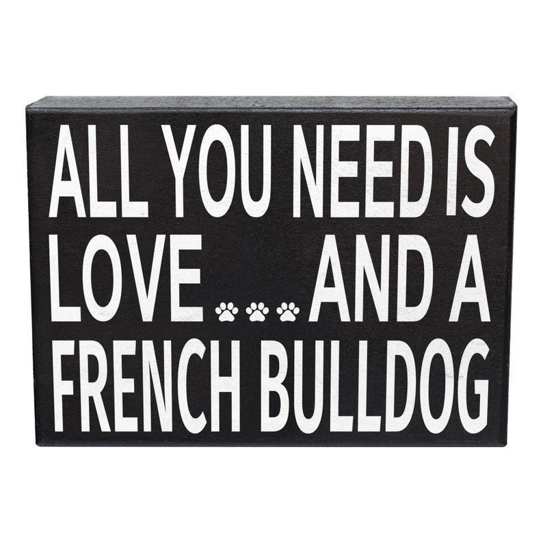 May include: Black wooden sign with white text that reads "All you need is love... and a French Bulldog".