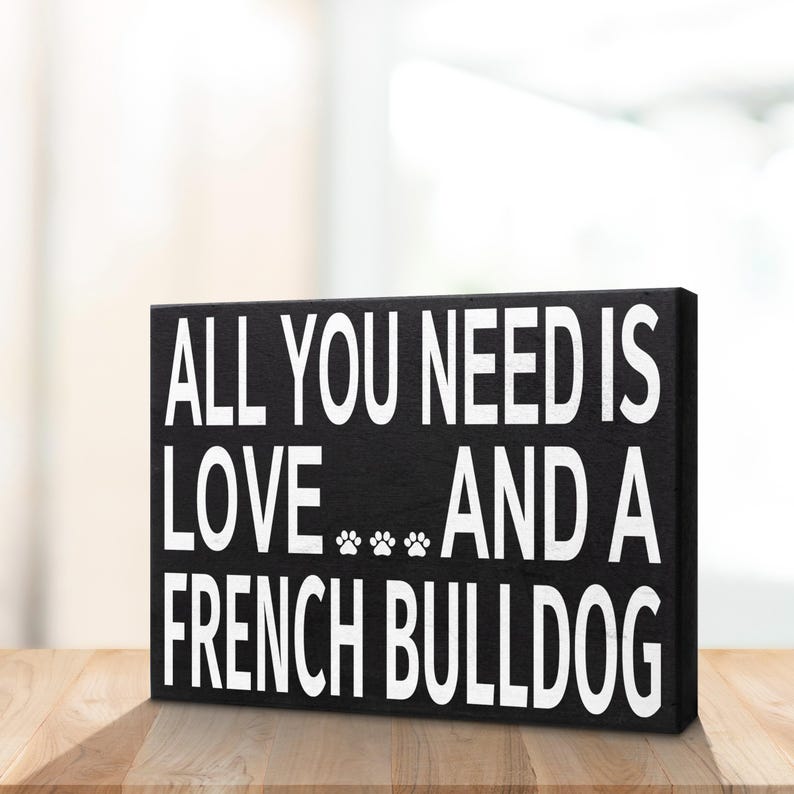 May include: Black wooden sign with white text that reads "All you need is love... and a French Bulldog".