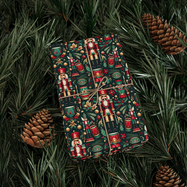 May include: A rectangular gift box wrapped in dark green paper featuring a repeating pattern of red and gold nutcrackers, drums, and small ornaments, tied with a thin brown twine string centered across the front of the package.