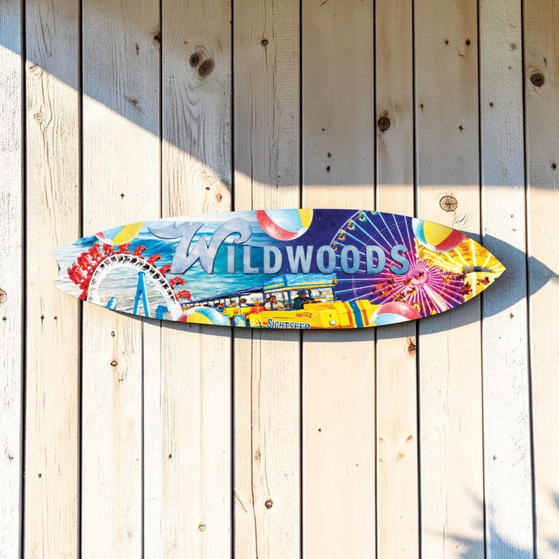May include: A colorful surfboard-shaped wooden sign with the word "Wildwoods" in white lettering. The sign features a vibrant illustration of a Ferris wheel, beach balls, and a bus. The sign is mounted on a weathered, light-colored wooden wall.