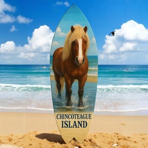 May include: A wooden surfboard with a painting of a brown and blonde horse standing in the ocean. The surfboard has the words "Chincoteague Island" printed on it.