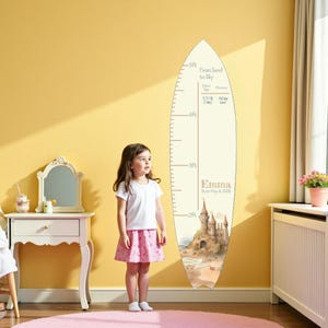 May include: A wooden growth chart in the shape of a surfboard, measuring up to 5 feet. The chart features a watercolor illustration of a castle on a beach. Text includes "From Sand to Sky" and "Emma Born May 4, 2026".