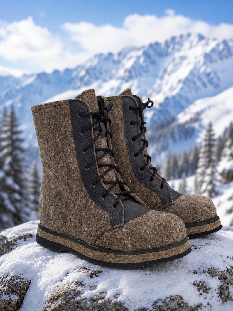 May include: A pair of brown felt winter boots with black leather accents and black laces. The boots are set against a snowy, mountainous backdrop, suggesting cold weather and outdoor activities.
