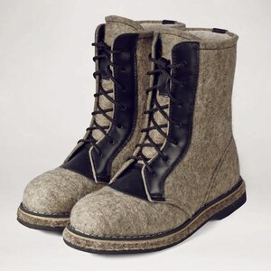 May include: A pair of gray felt boots with black leather accents and black laces. The boots have a sturdy sole and a high-top design, suitable for cold weather. The boots are made of a thick, textured material.