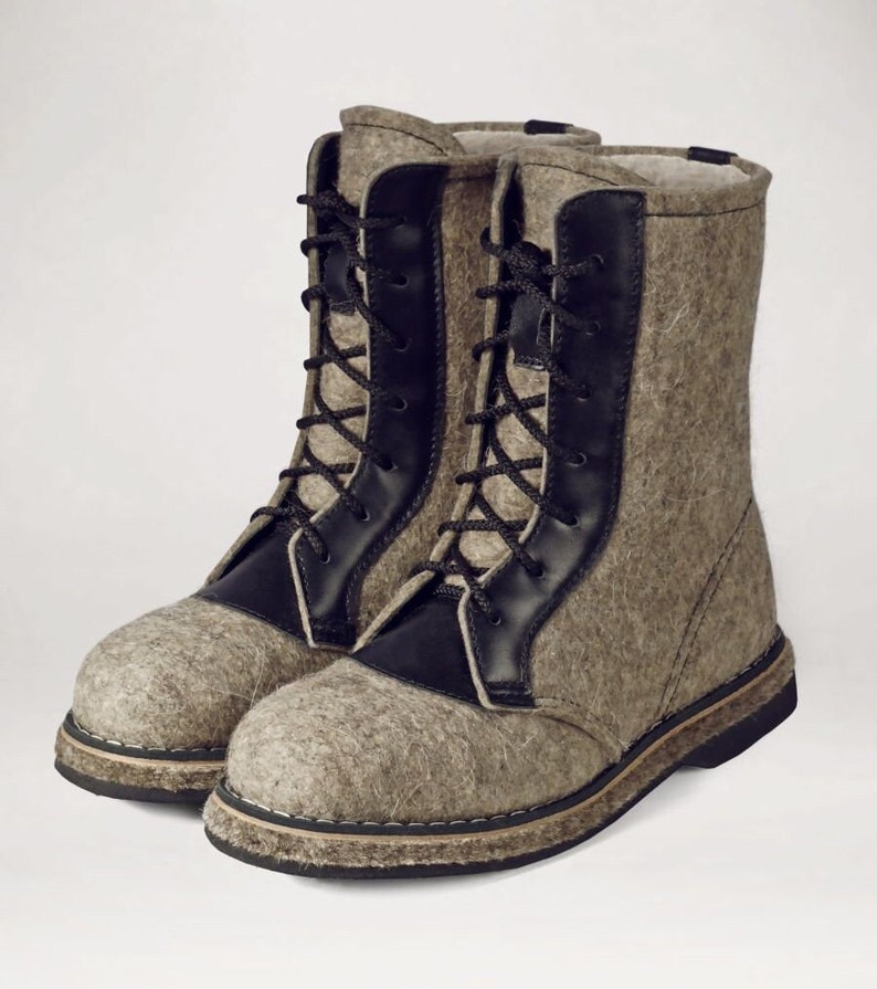 May include: A pair of gray felt boots with black leather accents and black laces. The boots have a sturdy sole and a high-top design, suitable for cold weather. The boots are made of a thick, textured material.