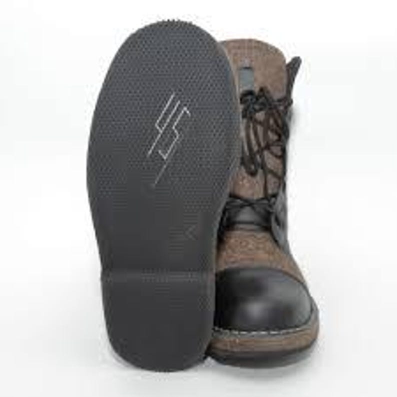 May include: A pair of ankle boots with a black leather toe and heel, and a brown fabric upper. The boots have black laces and a black rubber sole. The sole of one boot is facing the camera, displaying a white graphic.