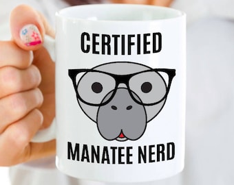 May include: White ceramic mug with a gray manatee wearing glasses and the text "CERTIFIED MANATEE NERD".