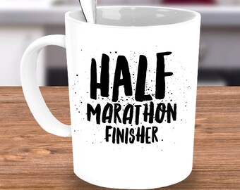 May include: White ceramic coffee mug with a black graphic that says "HALF MARATHON FINISHER".