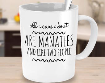 May include: White ceramic coffee mug with a black design that reads "all i care about are manatees and like two people".
