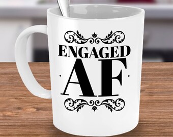 May include: White ceramic coffee mug with a black design that says "Engaged AF" with a decorative flourish above and below the text.