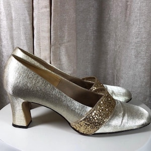 May include: A pair of gold satin pumps with a gold glitter accent on the toe. The heels are block heels.