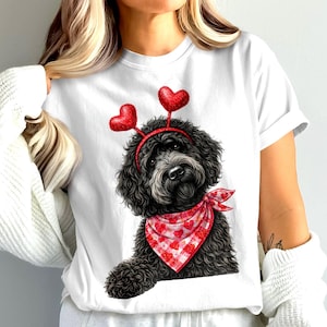 May include: White t-shirt featuring a black dog with a red heart-shaped headband and a red and white checkered bandana. The dog illustration has a Valentine's Day theme.