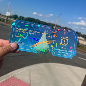 May include: A holographic blue ticket with a stylized illustration of a bird and text. The ticket has a unique shape with a notched edge and iridescent accents. The background is a clear blue sky.