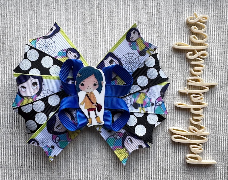 May include: A handmade hair bow featuring a cartoon character design. The bow is made of layered ribbons in black with white polka dots, and a patterned ribbon with a cartoon character and spiderwebs. A blue ribbon is in the center.