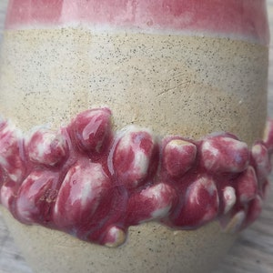 Puede incluir: Una taza de cerámica con un esmalte rosa y blanco. La taza tiene un diseño texturizado alrededor de la parte inferior, que se asemeja a un grupo de pequeñas flores rosas.