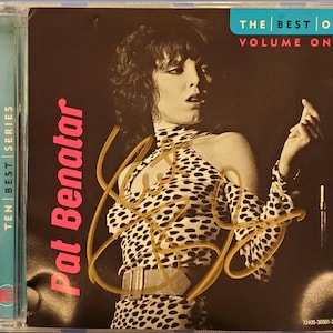 May include: A CD case with a black background featuring a photo of Pat Benatar in a black and white polka dot shirt. The text "The Best Of Volume One" is in the upper right corner. The text "Ten Best Series" is on the left side of the case. The CD case is signed by Pat Benatar.