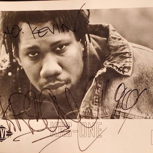May include: Black and white photo of a man with dreadlocks wearing a denim jacket. The man is looking at the camera and has a serious expression on his face. The photo is signed "To Kevin" and "KRS-ONE".