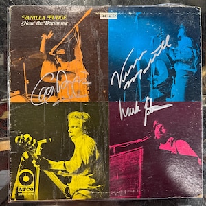 Puede incluir: Una portada de álbum de vinilo vintage con la banda Vanilla Fudge. El álbum se titula "Near the Beginning" y presenta un collage colorido de los miembros de la banda. La portada del álbum está firmada por cada miembro de la banda: Carmine Appice, Vince Martell, Mark Stein y Tim Bogert.