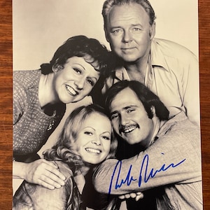 May include: A black and white photograph of four people smiling. The photograph is signed in blue ink. The people are two women and two men. The photograph is on a wooden surface.