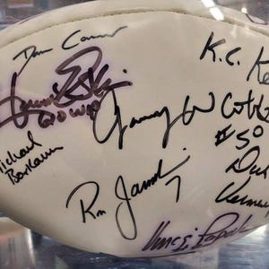 May include: White football with multiple black signatures, including "Don Carr", "K.C. Keeler", "Randy  Cotte #50", "Michael  Borlaum", "Ron  Jamont", and "Jim  Pope".