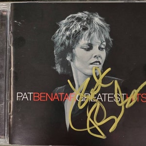 May include: A CD case featuring Pat Benatar's Greatest Hits album. The cover has a black background with a photo of Pat Benatar and her signature in gold. The album title is in white and red.