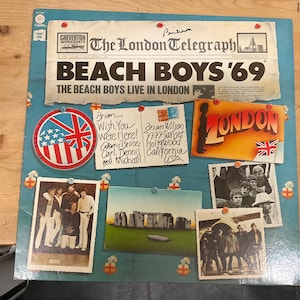 May include: A vintage record album cover featuring a collage of images related to the Beach Boys' 1969 concert in London. The cover features a red, white, and blue Union Jack flag, a photo of the band, and the text "Beach Boys '69" and "The Beach Boys Live in London".