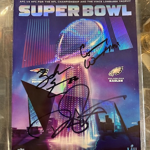 Könnte beinhalten: Ein Super Bowl-Spielprogramm vom 4. Februar 2018 mit den New England Patriots und den Philadelphia Eagles. Das Cover zeigt das Super Bowl-Logo, Teamlogos und Spielersignaturen. Das Programm befindet sich in einer Schutzhülle.