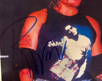 May include: A photograph of a person wearing a black tank top with a graphic design and blue jeans. The tank top features a white and blue image. The person has curly hair and a signature in blue ink.