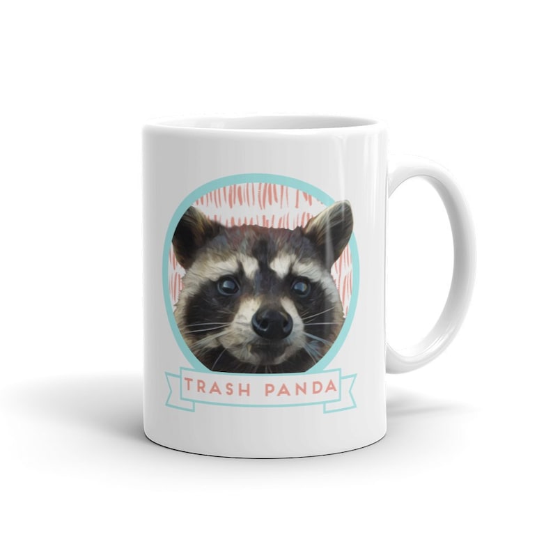 May include: White ceramic mug with a cartoon raccoon face and the text "Trash Panda" in a blue and white banner.