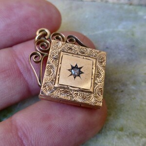 K&ouml;nnte beinhalten: Ein goldenes Medaillon mit einem sternf&ouml;rmigen Stein in der Mitte. Das Medaillon hat ein dekoratives, graviertes Design und eine Scharnier&ouml;ffnung.
