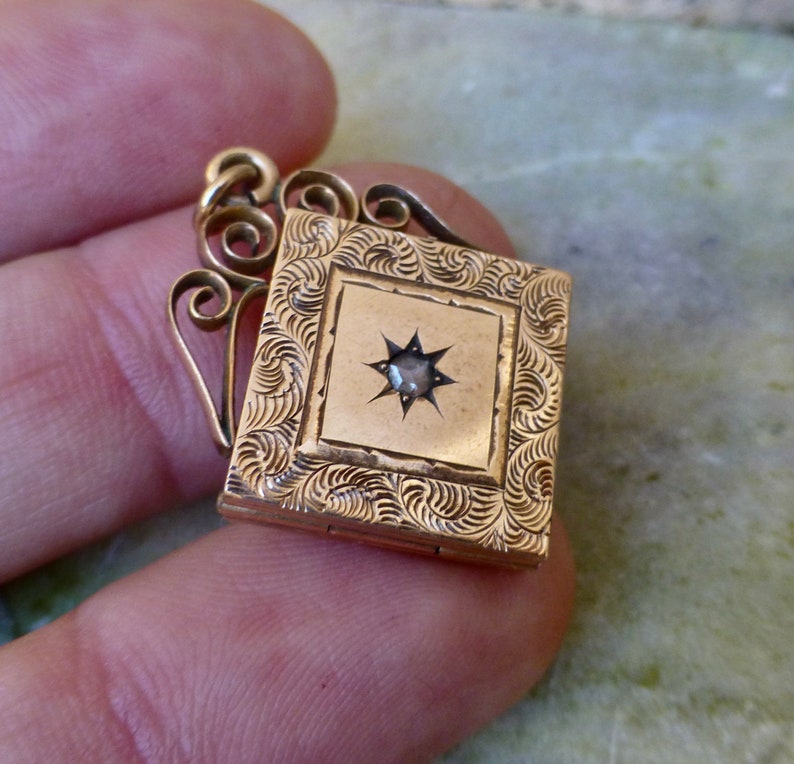 K&ouml;nnte beinhalten: Ein goldenes Medaillon mit einem sternf&ouml;rmigen Stein in der Mitte. Das Medaillon hat ein dekoratives, graviertes Design und eine Scharnier&ouml;ffnung.