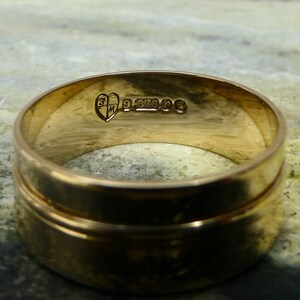 May include: A gold wedding band with a heart-shaped hallmark and the inscription "9 375" on the inside of the band.