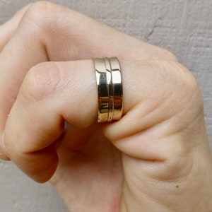 May include: A gold band ring with a double band design. The ring is worn on a person's finger.