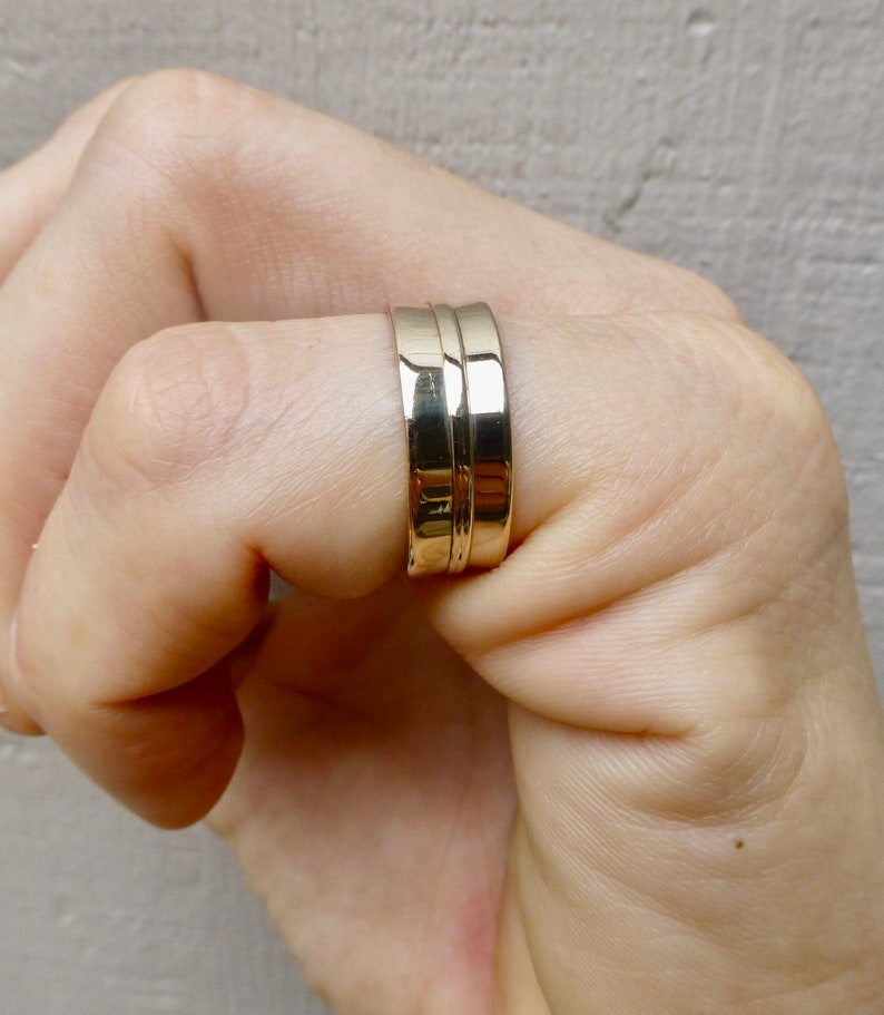 May include: A gold band ring with a double band design. The ring is worn on a person's finger.