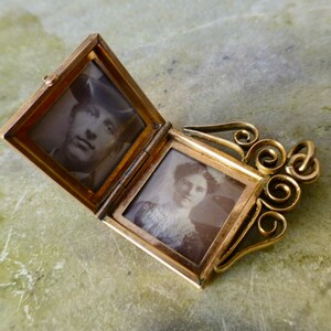 K&ouml;nnte beinhalten: Ein goldenes Medaillon mit einer Scharnier&ouml;ffnung, die zwei Schwarzwei&szlig;fotos von Personen enth&uuml;llt. Das Medaillon hat ein dekoratives, verziertes Design mit einer Schlaufe zum Anbringen einer Kette.
