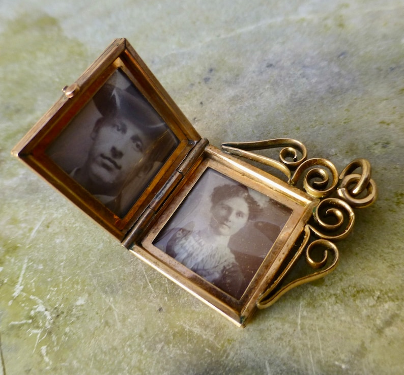 K&ouml;nnte beinhalten: Ein goldenes Medaillon mit einer Scharnier&ouml;ffnung, die zwei Schwarzwei&szlig;fotos von Personen enth&uuml;llt. Das Medaillon hat ein dekoratives, verziertes Design mit einer Schlaufe zum Anbringen einer Kette.
