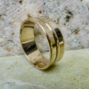 May include: A gold wedding band with a double groove design. The band is polished and has a smooth finish.