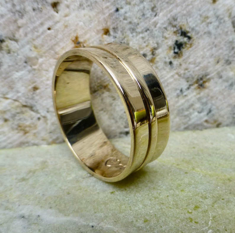 May include: A gold wedding band with a double groove design. The band is polished and has a smooth finish.