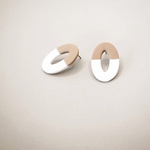 Puede incluir: Un par de pendientes ovalados de color blanco y beige. Los pendientes están hechos de un material liso y mate.