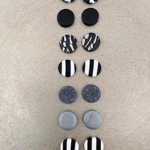 Könnte beinhalten: Eine Sammlung handgefertigter Ohrstecker in verschiedenen Designs. Die Ohrringe weisen schwarz-weiße Muster auf, darunter Streifen, abstrakte Linien und gesprenkelte Texturen. Die Ohrringe sind rund und haben eine minimalistische Ästhetik.