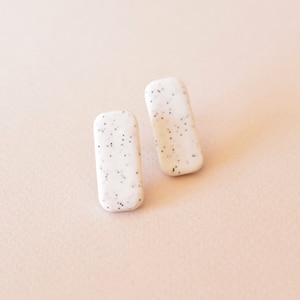 Könnte beinhalten: Ein Paar weiße rechteckige Ohrringe mit einem gesprenkelten schwarz-weißen Muster.