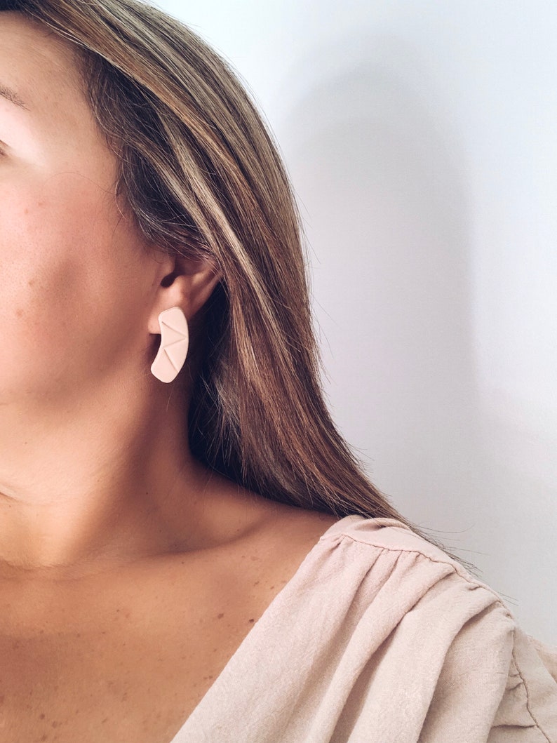 Model wearing modern minimalist beige stud earrings for size reference handmade from polymer clay by Vertseas.